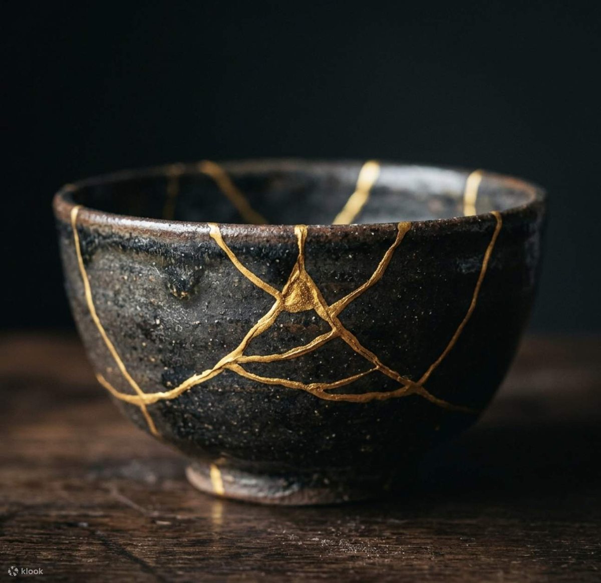 A dark tea bowl mended with gold seams, in the kintsugi way